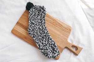 Close-up of cozy coral fleece socks with black pom-pom detail on a wooden surface