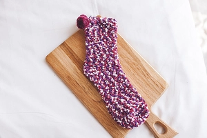 Detail of soft purple and pink coral fleece warm sock with small pompom on wooden board