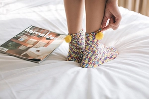 Cosy coral fleece socks with yellow pom-pom detail on bed for warm home lounging