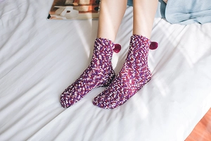 Detail of soft purple coral fleece socks with white polka dots and fuzzy pom-pom accents
