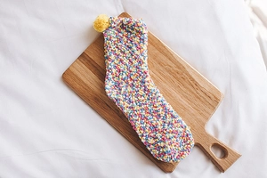 Close-up of colorful coral fleece socks with a cute yellow pom-pom on wooden board