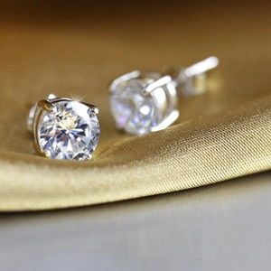 Macro detail of 925 silver stud earrings with high-gloss round zircons on silk background