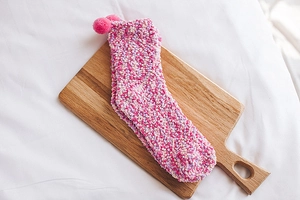 Pink coral fleece socks with pom-poms on a wooden board for winter comfort