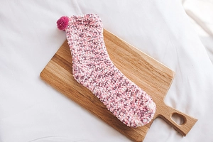 Detailed texture of pink and white coral fleece sock with decorative pom-pom on wood