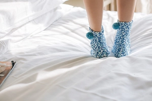 Detail of soft blue coral fleece warm socks with decorative pom-poms on cozy white bedding