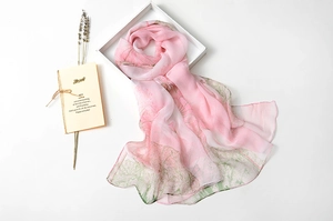 Detail of pink lotus silk scarf with green leaf pattern and elegant gift packaging