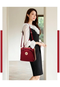 Detail of burgundy patent leather handbag with gold chain strap and metal decor