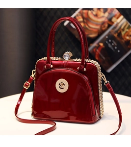 Detail of burgundy patent leather handbag featuring glossy finish and rhinestone clasp