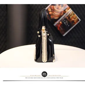 Side view of black patent leather handbag featuring rhinestone details and gold hardware