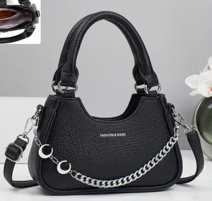 Detail of black pebbled leather crossbody bag with silver chain and crescent pendants