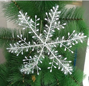 Close-up of white glitter snowflake hanging on green Christmas tree branch