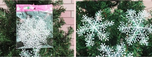 White glittery snowflake ornament in packaging and hanging on a green Christmas tree branch