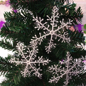 Close-up of white glittery plastic snowflake ornaments hanging on a green Christmas tree