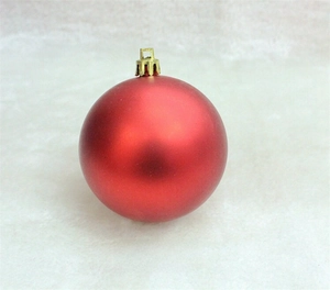 Detail of a 3cm red matte Christmas ball ornament with golden cap on grey velvet surface