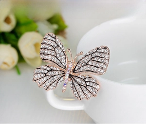 Exquisite butterfly brooch with white rhinestones on rose gold base pinned on a white cup