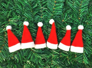Detailansicht von sechs roten Mini-Weihnachtsmützen aus Filz auf grünem Tannenzweig-Hintergrund
