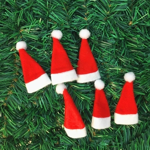 Gros plan de 6 mini bonnets de Noël rouges en peluche sur des branches de sapin vert
