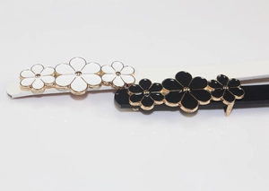 Detail of white and black PU leather belts with gold-rimmed floral snap buckles