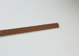 Detail view of a slim brown patent leather strap with white edge painting and round punch hole