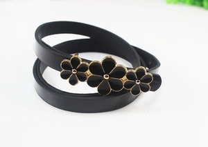 Close-up of a slim black faux leather belt featuring three gold-toned floral buckles