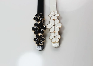 Detailed view of black and white skinny belts with floral buckle and gold trim accents