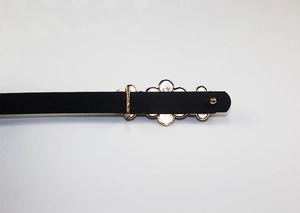 Detail view of a black patent leather belt with a golden flower metal buckle