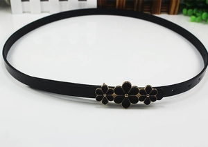 Close-up of a black skinny leather belt featuring a golden floral buckle on a white surface