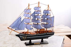 Vue détaillée du voilier miniature en bois avec voiles à rayures bleues et chaîne d'ancre dorée