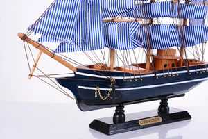 Détail d'une maquette de voilier en bois avec coque bleue et voiles en toile sur socle