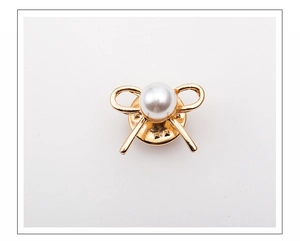 Detail of a golden bow brooch with a central white pearl on a clean white background