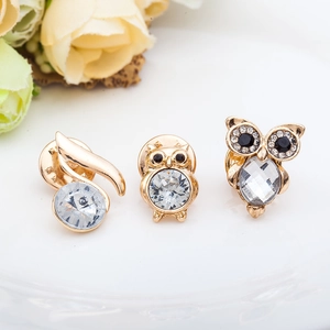 Three-piece gold-tone owl brooches set with clear and black crystals on a white plate