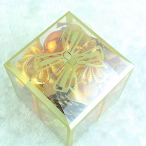 Macro detail of bronze Christmas ornaments in a transparent box on white plush fabric