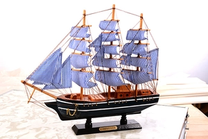 Detail of wooden sailboat model with blue striped sails and black hull on stand