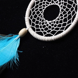 Detail of handmade dreamcatcher featuring white woven net, wooden bead and blue feather