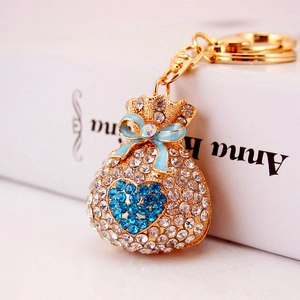 Golden money bag keychain with blue crystals and heart design on white background