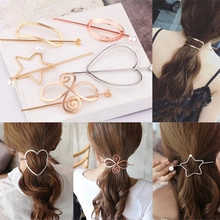 Detail view of geometric metal hair pins including heart and spiral shapes in gold finish