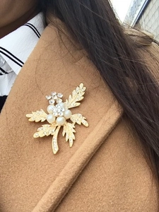 Close-up of a gold flower brooch with white pearls and rhinestones on a beige coat