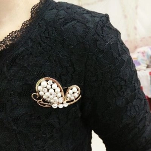 Detailed view of a golden butterfly brooch with white pearls on black lace fabric