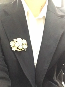 Elegant gold flower brooch with white petals and pearls on a black suit lapel