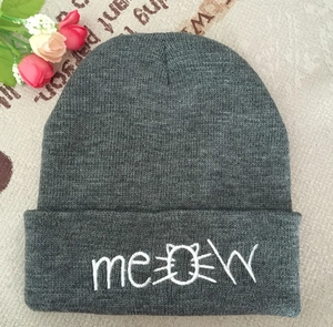 Detail of grey knitted beanie featuring white 'meow' embroidery with cute cat face