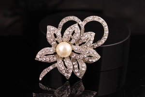 Detailed macro view of a silver flower brooch with a large pearl and sparkling rhinestones