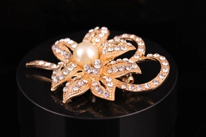 Macro detail of silver flower brooch featuring white rhinestones and large pearl center