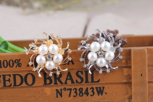 Dettaglio di spille a fiore con perle e strass color oro e argento su base di legno
