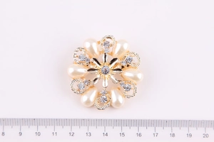 Vista macro di una spilla a fiore dorata da 4,5 cm con perle e strass su sfondo bianco