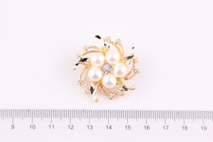 Dettaglio della spilla a corona con perle e cristalli accanto a un righello da 4 cm