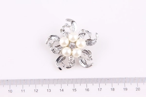 Dettaglio di una spilla a fiore argento con perle e strass accanto a un righello