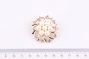 Dettaglio di una spilla a fiore dorata con perle e cristalli con diametro di 4 cm