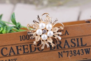 Macro di una spilla a fiore dorata con perle bianche e centro in strass scintillante