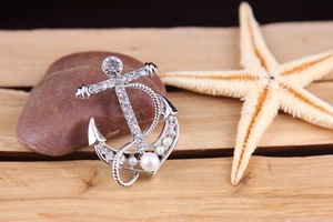 Detailed close-up of a silver rhinestone pearl anchor brooch on wood. Marine themed jewelry.