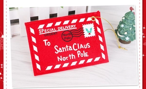 Detail of red felt Christmas envelope ornament with golden string on white wood background